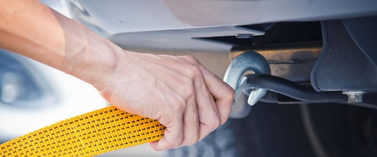 A man attaching a tow hook with a yellow recovery strap to a vehicle
